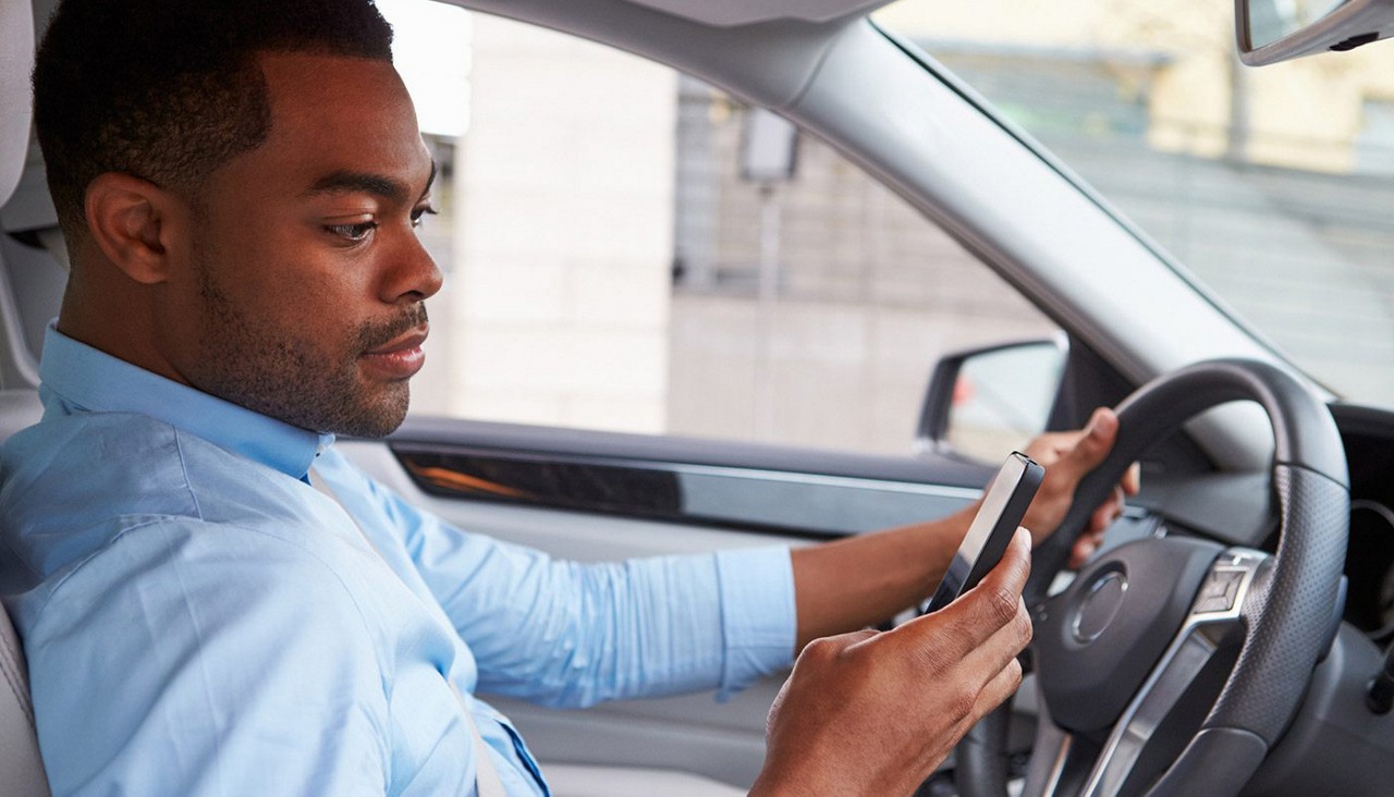 A man looking at his phone while in the driver's seat of his car.