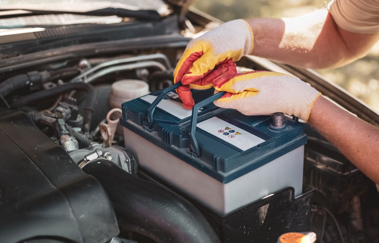A mechanic removing a car battery from the engine.