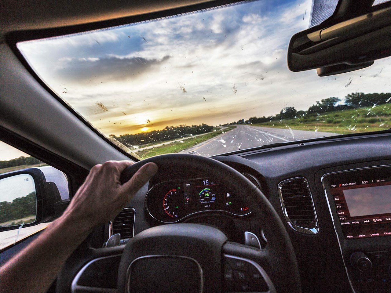 A close-up view of a person driving and the car windshield is covered in bug splatter.