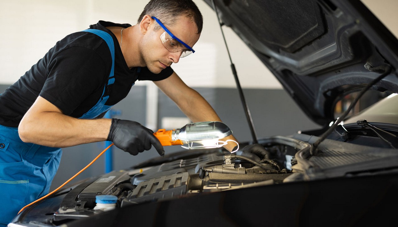 A mechanic with the car hood inspecting the engine with a spotlight.