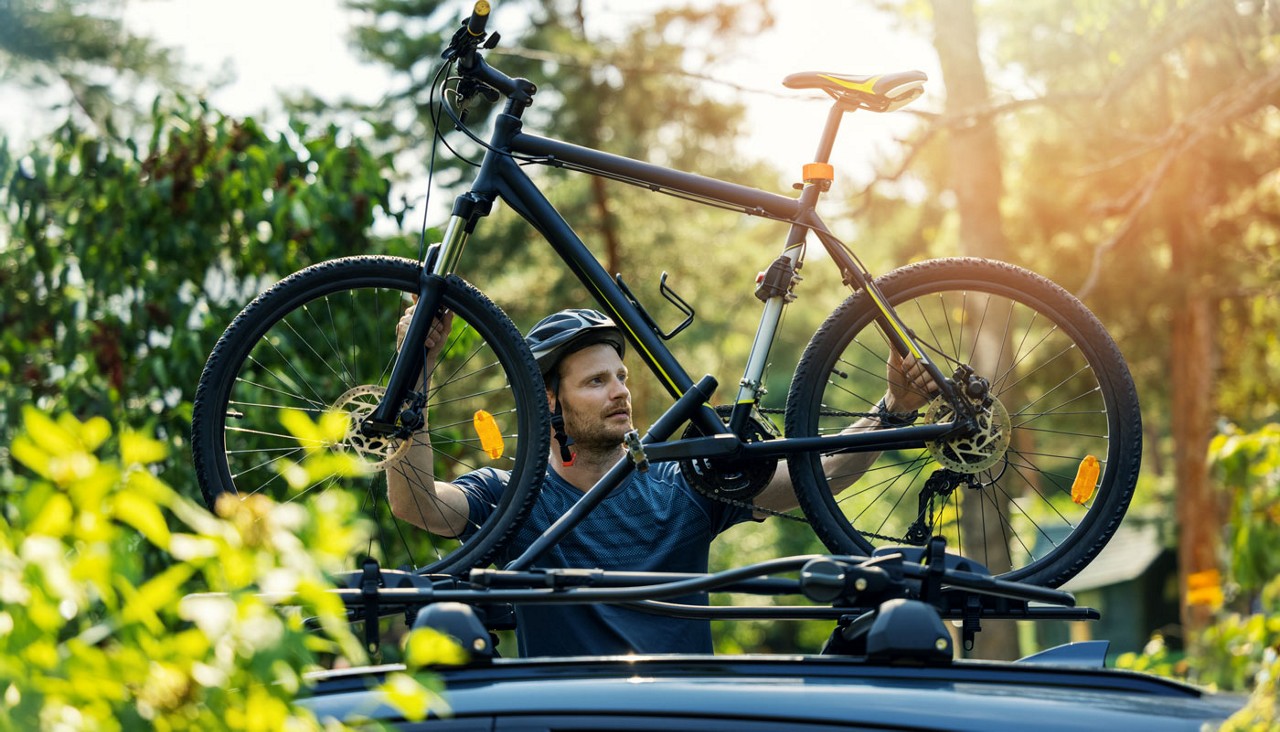 A man lifting a bicycle onto a roof rack on his car.