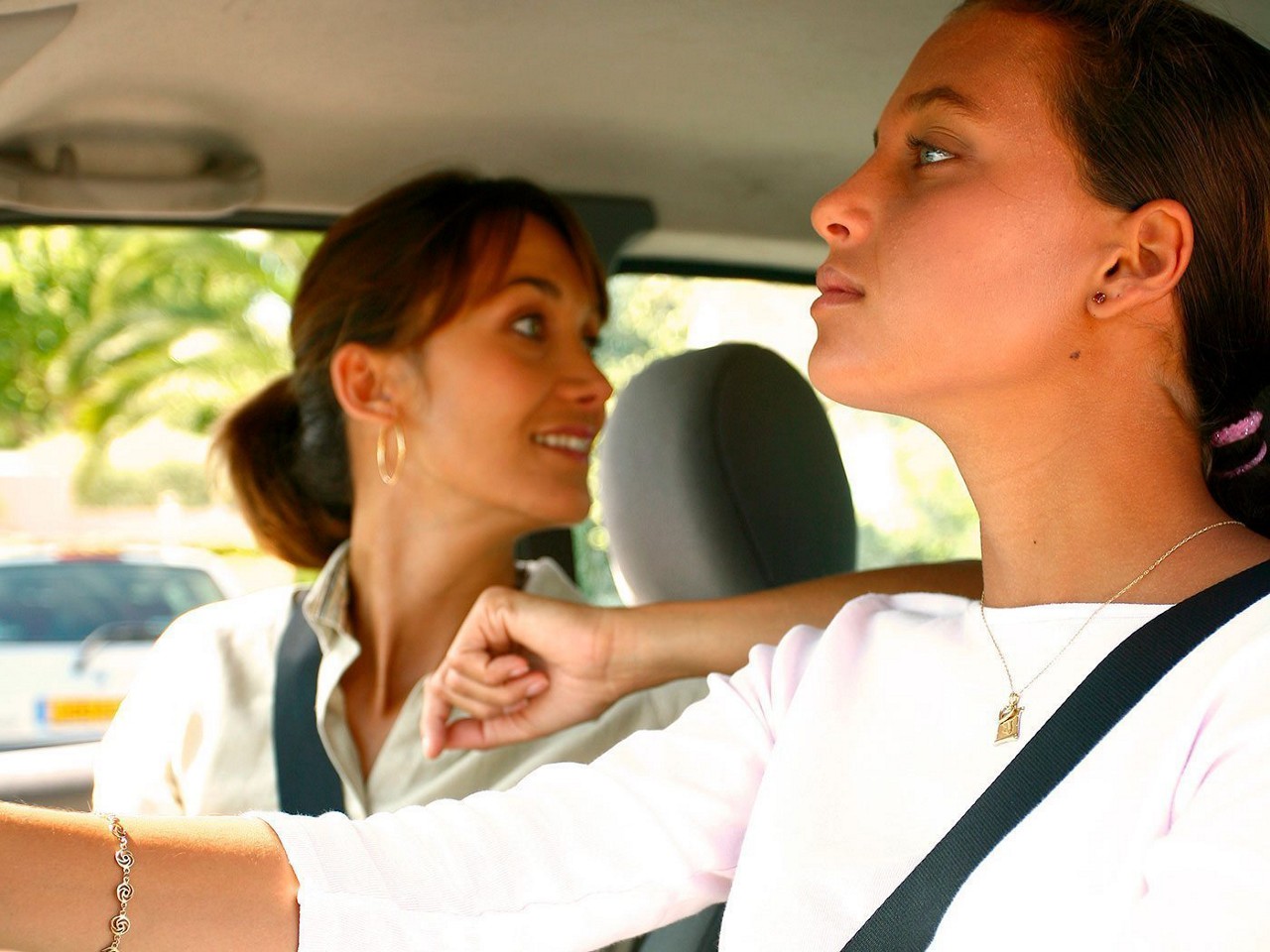 A mother in the passenger's seat teaching her daughter to drive.