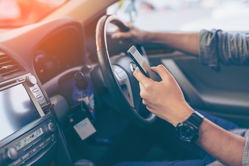 A close-up view of a man driving while texting on a phone.