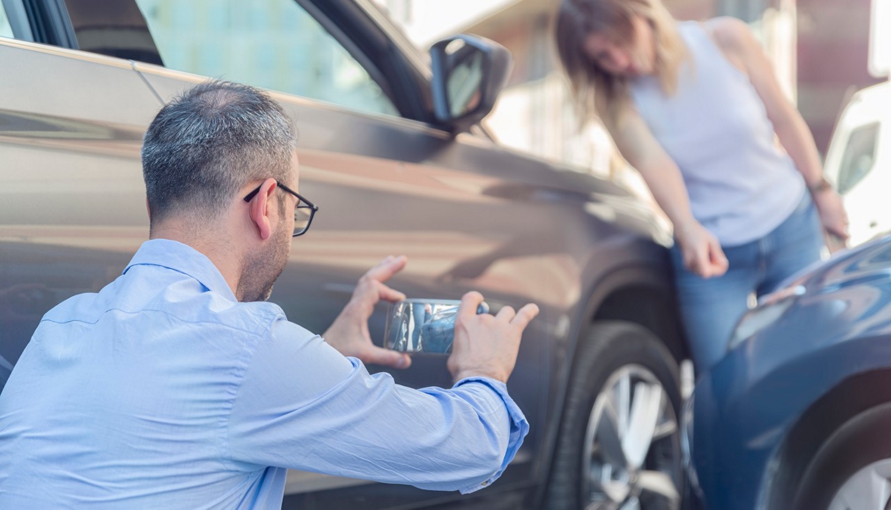 An insurance adjuster taking a picture of car damage while a young woman looks at her car against the other car.