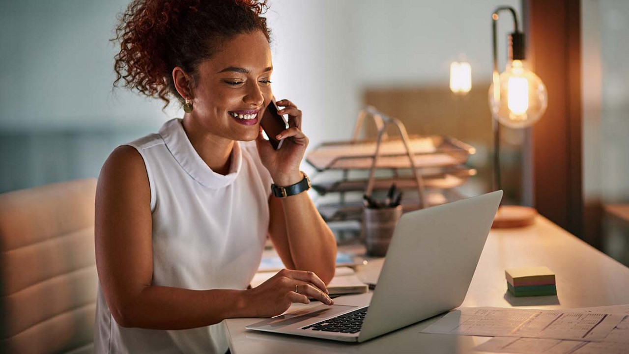 Shot of a cheerful young businesswoman taking a phone call while working late in her office