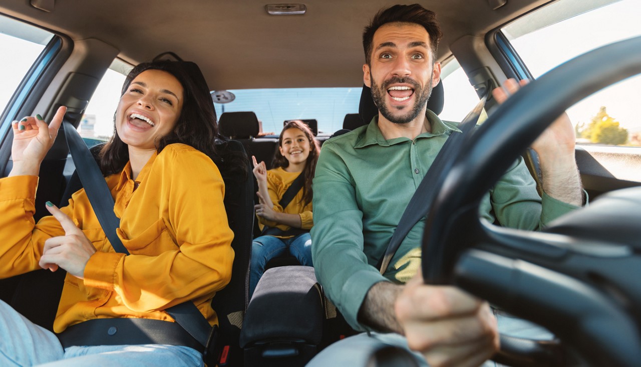 Happy family of three driving in their automobile, dancing to music and singing